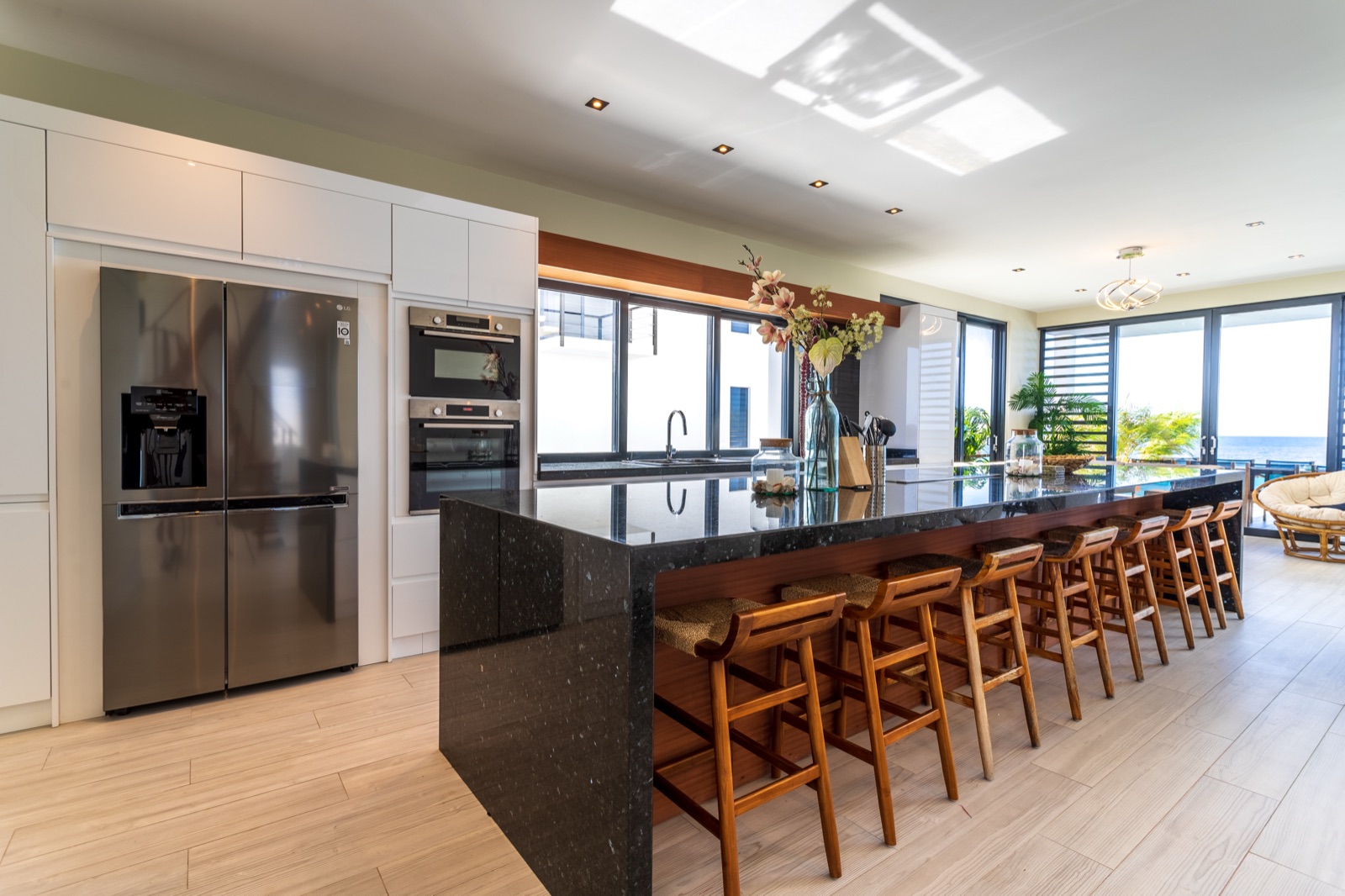 Luxury Bonaire villa gourmet kitchen with a black granite waterfall island, wood bar stools, stainless steel appliances, and a panoramic ocean view.